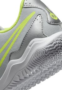 Zapatilla deportiva gris con una parte superior texturizada, acentos en verde neón y una suela de goma blanca que presenta un patrón de banda de rodadura en capas.