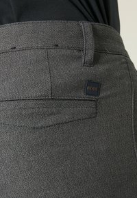 Grå vävda byxor med en subtil textur, bakficka och en fyrkantig logotyp med "BOSS" präglad. Rak skärning.