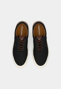 Sorte casual sneakers med brune snørebånd og indlægssåler, hvide såler og "JACK & JONES" branding indeni, vist fra oven på hvid baggrund.