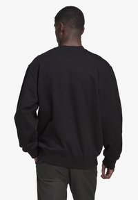 Svart sweatshirt med rund halsringning, sänkt axelsöm, ribbade ärmslut och nederkant, tillverkad av mjukt material. Sedd bakifrån.