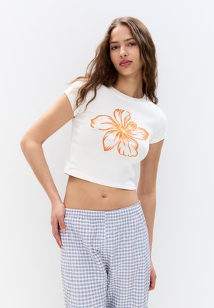 White cropped t-shirt with an orange flower print on the front, paired with light blue and beige checkered pants. Smooth fabric, short sleeves.