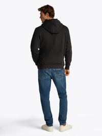 Felpa nera con cappuccio dal fit morbido, abbinata a jeans in denim blu con tasche posteriori. Completata con sneakers bianche.