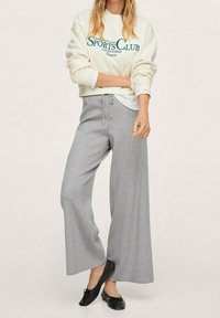 Pantaloni della tuta grigio chiaro a gamba larga con vita elastica e coulisse. Abbinati a una felpa color crema con scritta sportiva verde scuro.