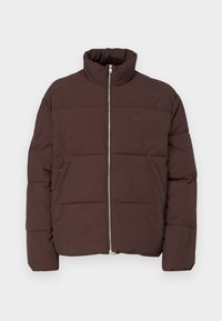 Doudoune marron avec un col haut, fermeture éclair à l'avant et deux poches latérales. Caractéristiques d'un design matelassé et d'un subtil détail de logo.