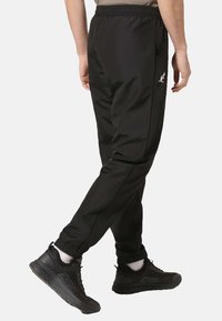 Pantaloni sportivi neri realizzati in tessuto liscio con cintura elastica e tasche laterali. Presentano un logo discreto sull'anca.