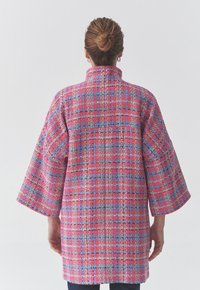 Manteau en tweed tissé dans des tons de rose, bleu et or ; il présente un col haut, des manches larges et une coupe décontractée. Motif texturé sur l'ensemble.