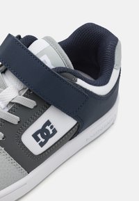 Basket grise et marine avec des accents blancs, présentant une tige texturée, une sangle à boucle et un col rembourré pour le confort.