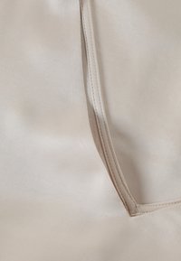 Beige satiinikangas, jossa on sileä pinta, hienovarainen tikkaus reunassa ja kevyt kiilto.