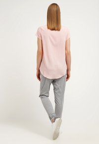 Top a maniche corte rosa chiaro con orlo arrotondato abbinato a pantaloni sportivi grigi. Il modello indossa scarpe da ginnastica bianche. Tessuto liscio con una vestibilità casual.