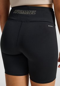 Svarta cykelshorts med hög midja, med "HUMMEL"-logotyp i vitt och en liten "BECOOL"-etikett på sidan. Mjuk textur.