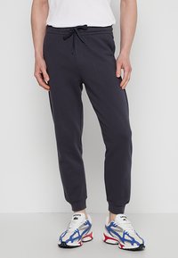 Marineblauwe joggingbroek van zachte stof met een elastische tailleband, verstelbaar trekkoord en ribbels bij de boorden. Gecombineerd met witte en blauwe sneakers.