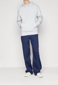 Ljusblå hoodie med framficka, kombinerad med marinblå byxor och vita sneakers, allt i en avslappnad och ledig passform.