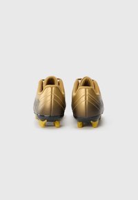 Gullfargede fotballsko med en glatt finish, med svart såle og gule knotter, designet med elegante linjer og minimal merkevareprofil på baksiden.
