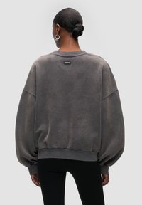 Sudadera de gran tamaño en gris oscuro con un acabado texturizado, hombros caídos y puños acanalados, con una pequeña etiqueta de logo en la parte de atrás.