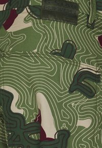 Tissu vert et beige à motif avec des lignes topographiques abstraites et des formes vert foncé, avec une poche cousue et une étiquette en denim G-Star Originals.