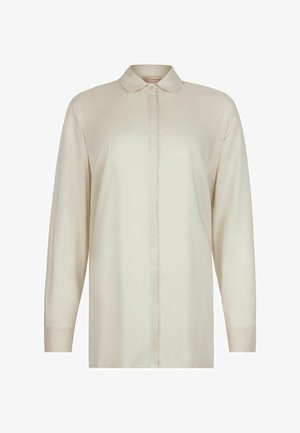 Langes, cremefarbenes Hemd mit verdeckter Knopfleiste und spitzem Kragen, frontal auf weißem Hintergrund präsentiert.
