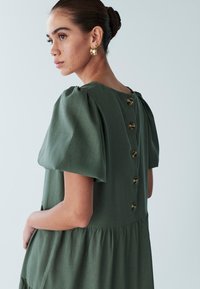 Roheline volangidega kleit kihilise seelikuga ja nööpidega tagaküljel. Valmistatud tekstureeritud kangast, suurte ümarsuuruste nööpidega kaunistatud.