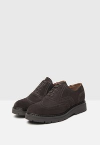 Scarpe derby in suede grigio scuro con un design tradizionale a brogue, caratterizzate da dettagli perforati e una robusta suola in gomma nera.