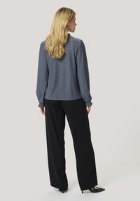 Blusa blu a maniche lunghe con motivo testurizzato, caratterizzata da polsini arricciati e una vestibilità rilassata, abbinata a pantaloni larghi neri.