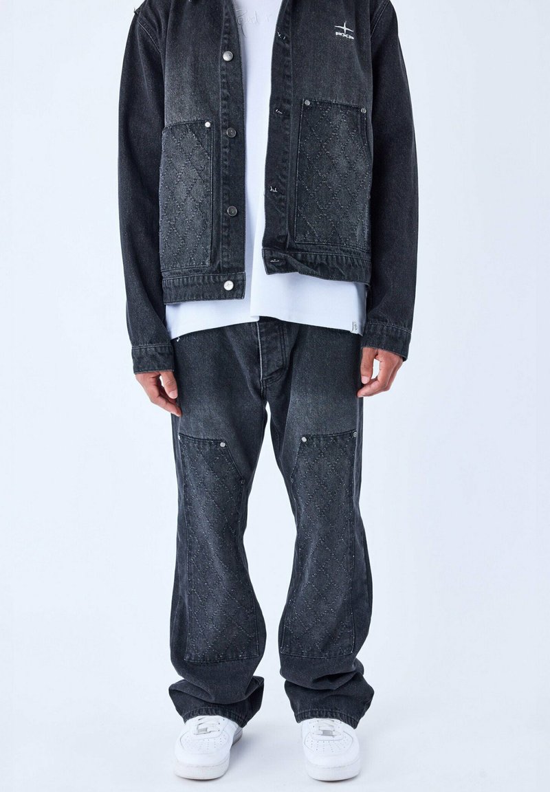 Conjunto de chaqueta y pantalones de mezclilla negra con bolsillos acolchados, herrajes plateados y un corte relajado, combinado con zapatillas blancas.
