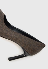 Zapato de tacón alto con diseño marrón, punta puntiaguda, material sintético texturizado y un tacón negro elegante de aproximadamente 7 cm de altura.