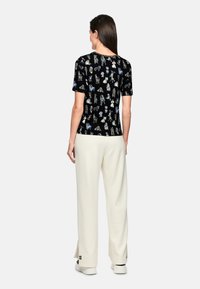 Short-sleeve black shirt featuring colorful dog illustrations. Paired with loose, cream-colored pants with side slits and white footwear.