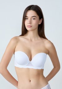 Reggiseno bianco senza bretelle con superficie liscia, rifinitura in pizzo lungo il bordo inferiore e texture morbida. Presenta una coppa a forma di cuore per il sostegno.