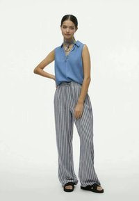 Camisa sin mangas azul claro combinada con pantalones anchos a rayas grises y blancas. Sandalias con una tira negra. Diseño simple, estilo casual.