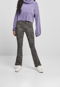 Lila gestrickter Pullover mit Rollkragen und langen Ärmeln, kombiniert mit schwarz-weißem Zebra-Print im Schlaghosen-Stil, getragen mit weißen Sneakers.