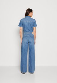 Denim kombinezon v светлозеlem, z zasnovo s ovratnikom, kratkimi rokavi, širokimi hlačnicami in zadnjim žepom z oznako blagovne znamke.