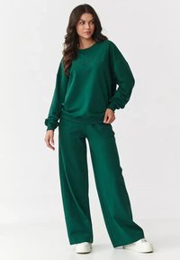 Zielony, oversize'owy sweter z haftowanym napisem i pasującymi szerokimi spodniami dresowymi. Wykonany z miękkiego materiału, z długimi rękawami i luźnym krojem.