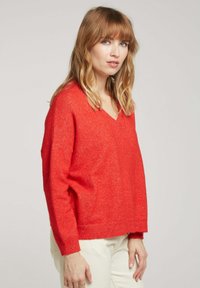 Pull rouge à col en V avec une coupe décontractée, fabriqué en tissu doux et texturé. Épaules tombantes, poignets et ourlet côtelés. Design minimaliste, sans motifs.