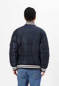 Námornícka puffer bunda s horizontálnymi sekciami, rebrovaný biely a čierny golier a manžety, spojená so svetlomodrými džínami. Hladká textúra.