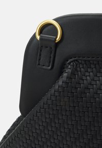 Czarna pleciona torba z teksturowanym korpusem, górą z gładkiej skóry i złotym metalowym pierścieniem. Kompaktowy, nowoczesny design o czystych liniach.