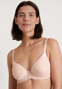 Lichtroze beha met kantdetails langs de onderrand, gladde cups, verstelbare bandjes en een haaksluiting aan de achterkant.