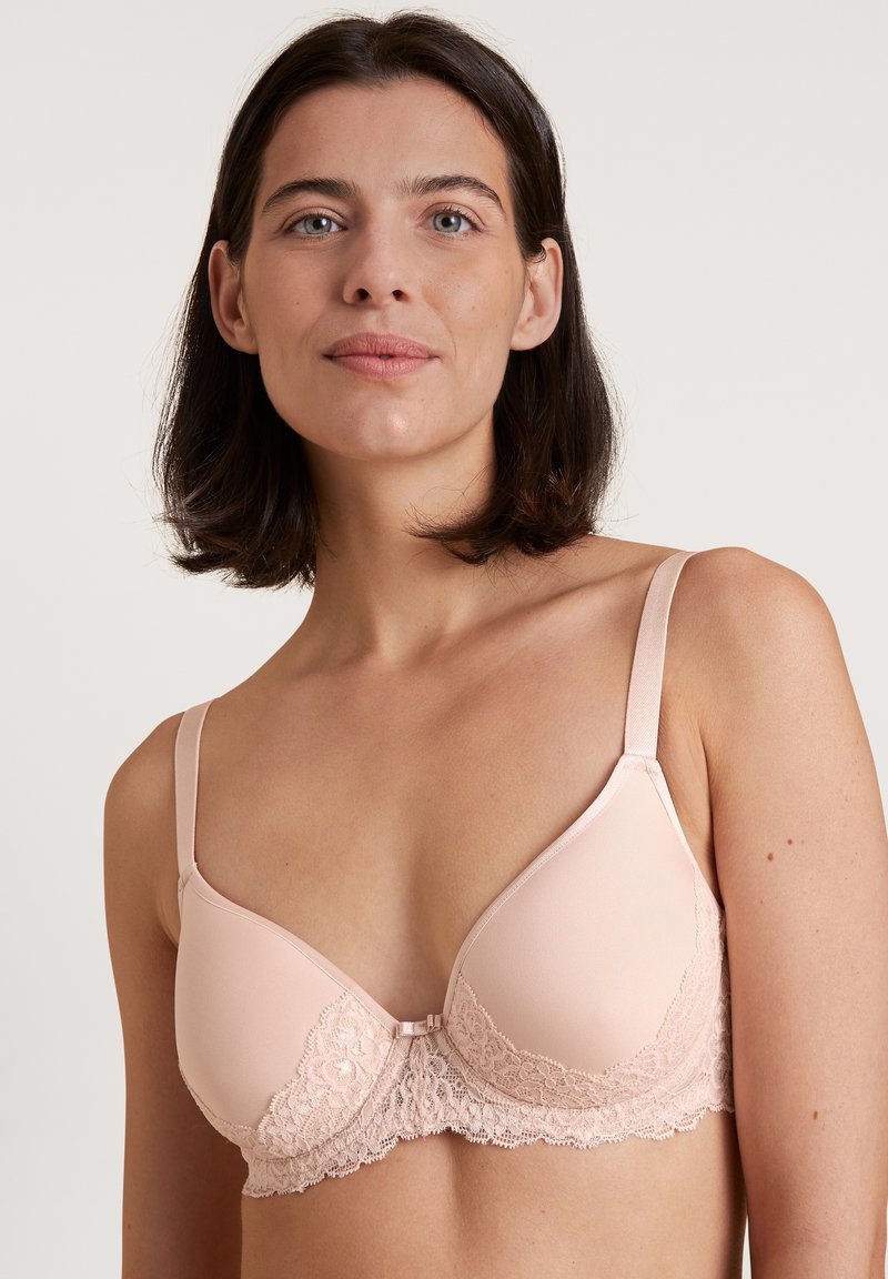 Lichtroze beha met kantdetails langs de onderrand, gladde cups, verstelbare bandjes en een haaksluiting aan de achterkant.