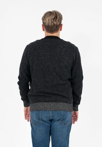 Maglione lavorato a maglia grigio scuro con scollatura rotonda, polsini e orlo a costine. Indossato con jeans blu, che mostrano un tessuto testurizzato.