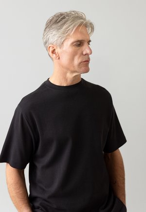 T-shirt nera a maniche corte realizzata in un materiale morbido, con scollatura rotonda e vestibilità rilassata, presentata su uno sfondo neutro.