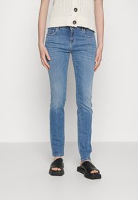 Ljust blå denimjeans med slim fit, lätt blekning på låren, femfickdesign, ihopparade med svarta slidesandaler på en neutral bakgrund.