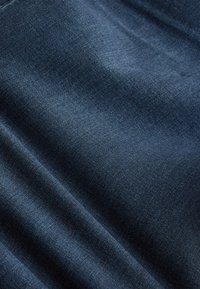 Dunkelblauer Denimstoff mit sichtbarer diagonaler Webstruktur und weichen Falten, die subtile Schatten erzeugen.