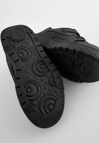 Chaussures noires avec une semelle en caoutchouc texturé présentant des motifs circulaires et des bords striés. Tige en matériau lisse avec des accents cousus.