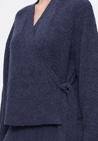 Maglione avvolgente blu navy in materiale a maglia texturata, con scollatura a V, maniche lunghe e cintura regolabile legata in vita.