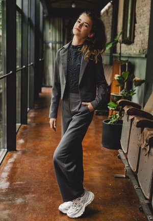 Grijze op maat gemaakte traje met een cropped blazer en wijde broek, gecombineerd met een zwart patroon top en witte sneakers. Voor een soepele stoftextuur.