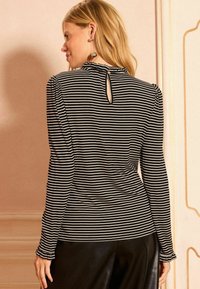 Fekete és fehér csíkos, hosszú ujjú felső, kulcslyuk hátkivágással, ráncolt vállakkal és fitted dizájnnal, texturált anyagból.