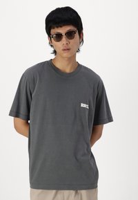 Camiseta de algodón gris con cuello redondo y mangas cortas. Presenta un pequeño logotipo blanco en el lado izquierdo del pecho y un corte holgado.