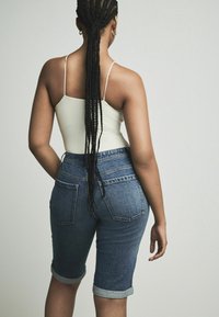 Shorts de mezclilla de talle alto con dobladillos enrollados, lavado azul y dos bolsillos traseros. Combinados con una camiseta sin mangas blanca ajustada.