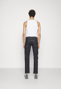 Mörkblå denimjeans med rak benstil, bärs med en vit linne; har en läderlapp på midjan och kontrasterande sömnad.