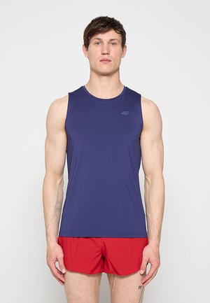 Homme athlétique debout face à l'avant, portant un débardeur bleu marine et un short de course rouge sur un fond blanc uni.