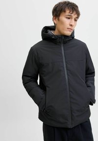 Černá izolovaná bunda s kapucí, předním zipem, bočními kapsami a hladkým matným povrchem. Minimalistický design s elegantním siluetou.