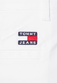 Hvit stoff med et rektangulært marineblått felt som har påskriften "TOMMY JEANS" i hvite og røde bokstaver, med en rød og hvit boksakcent.